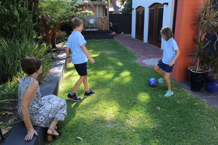 The two children kick a ball as their mother watches on.