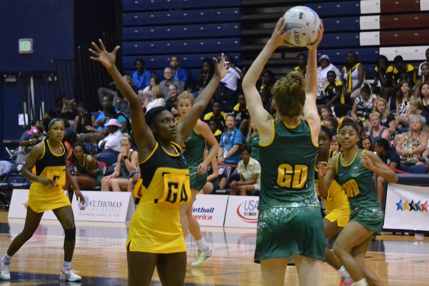 An Australian player holds the ball over head as she looks to pass to someone on court