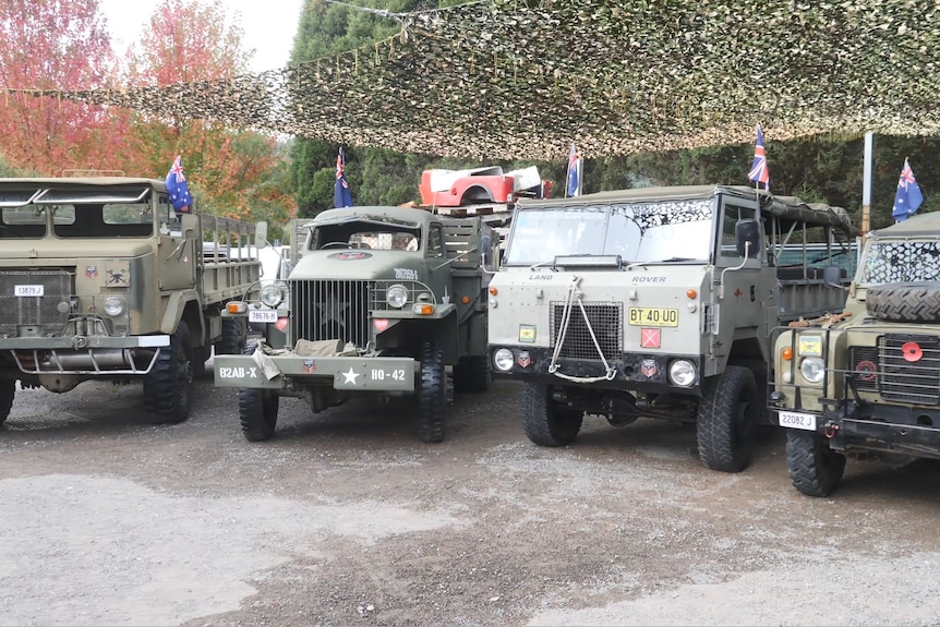 Four military trucks parked alongside each other with Australian flags poked into them.