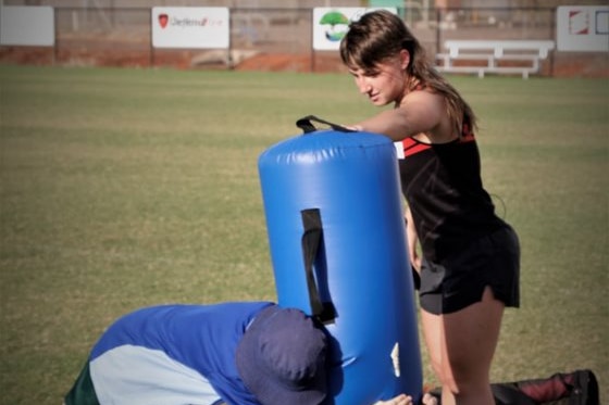 Phoebe Caudill holds tackling training equipment for a youth on a sport field. 