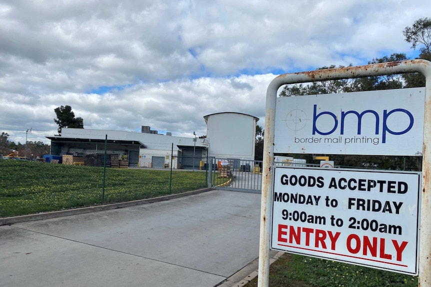 close up of sign with a white factory in the background