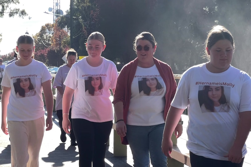 A group of young woman walking, wearing t-shirts with a woman's photo and the words "Her name is Molly".