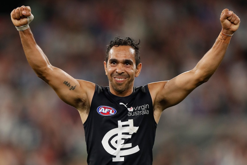 Man standing with his arms in the air smiling during a game of AFL