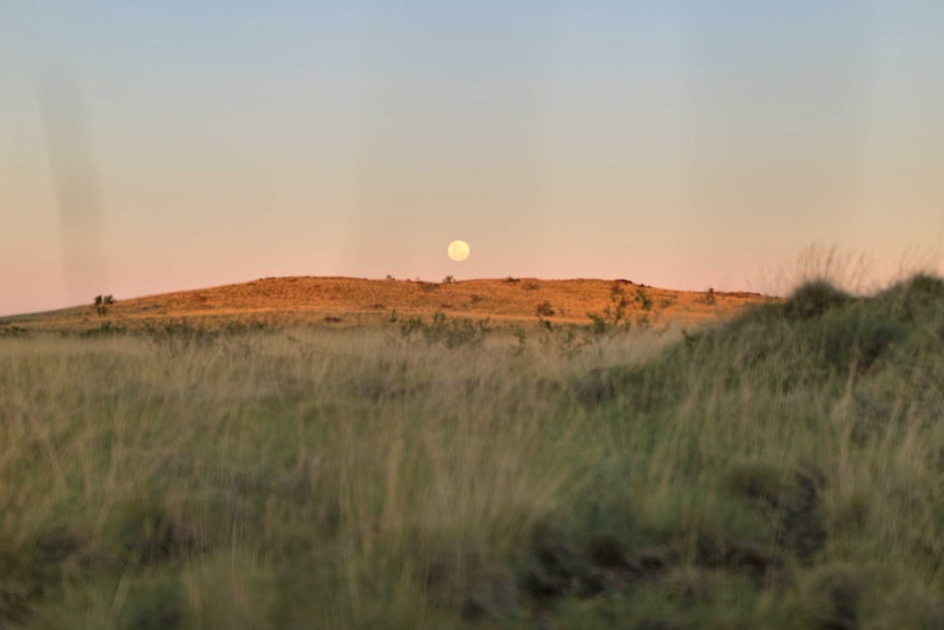 The moon disappears over a hill in WA's remote Murchison region as the sun rises.
