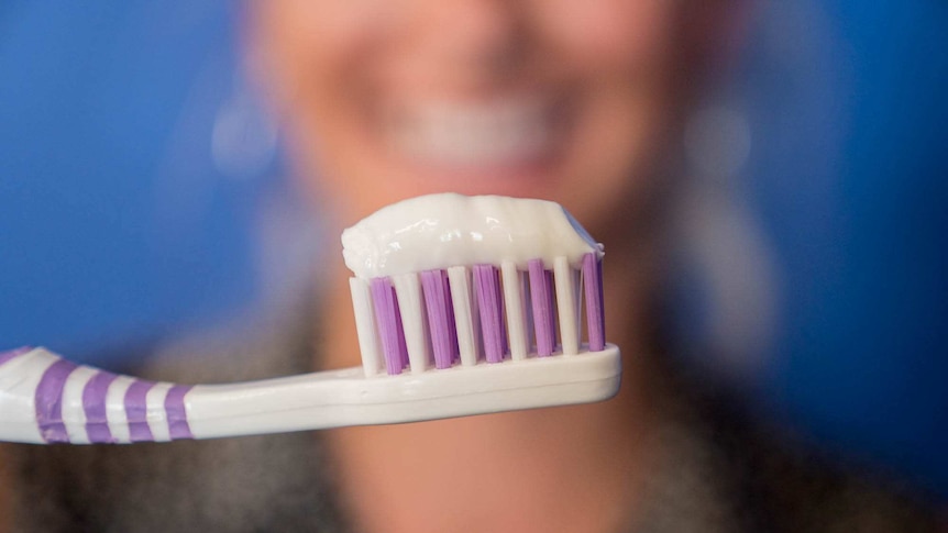 A woman holds a toothbrush with toothpaste while smiling