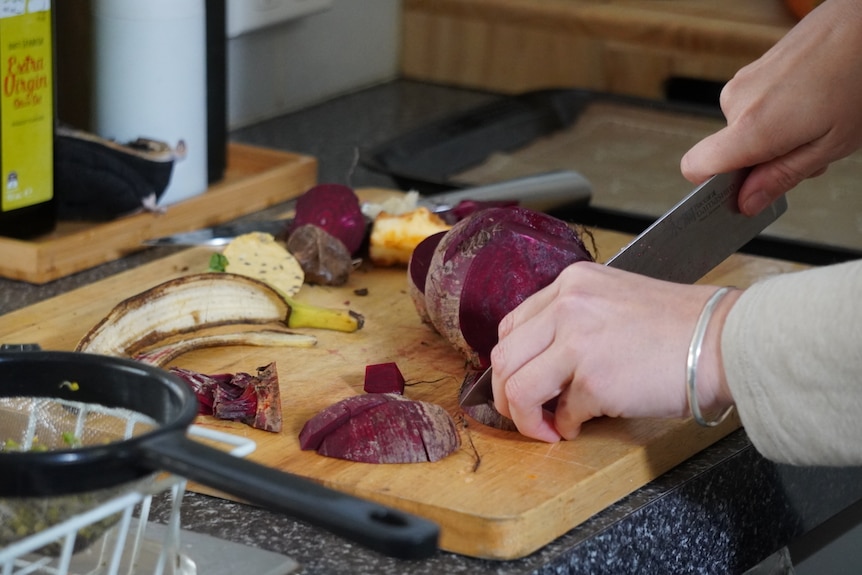 A hand is cutting a beetroot on a wooden board