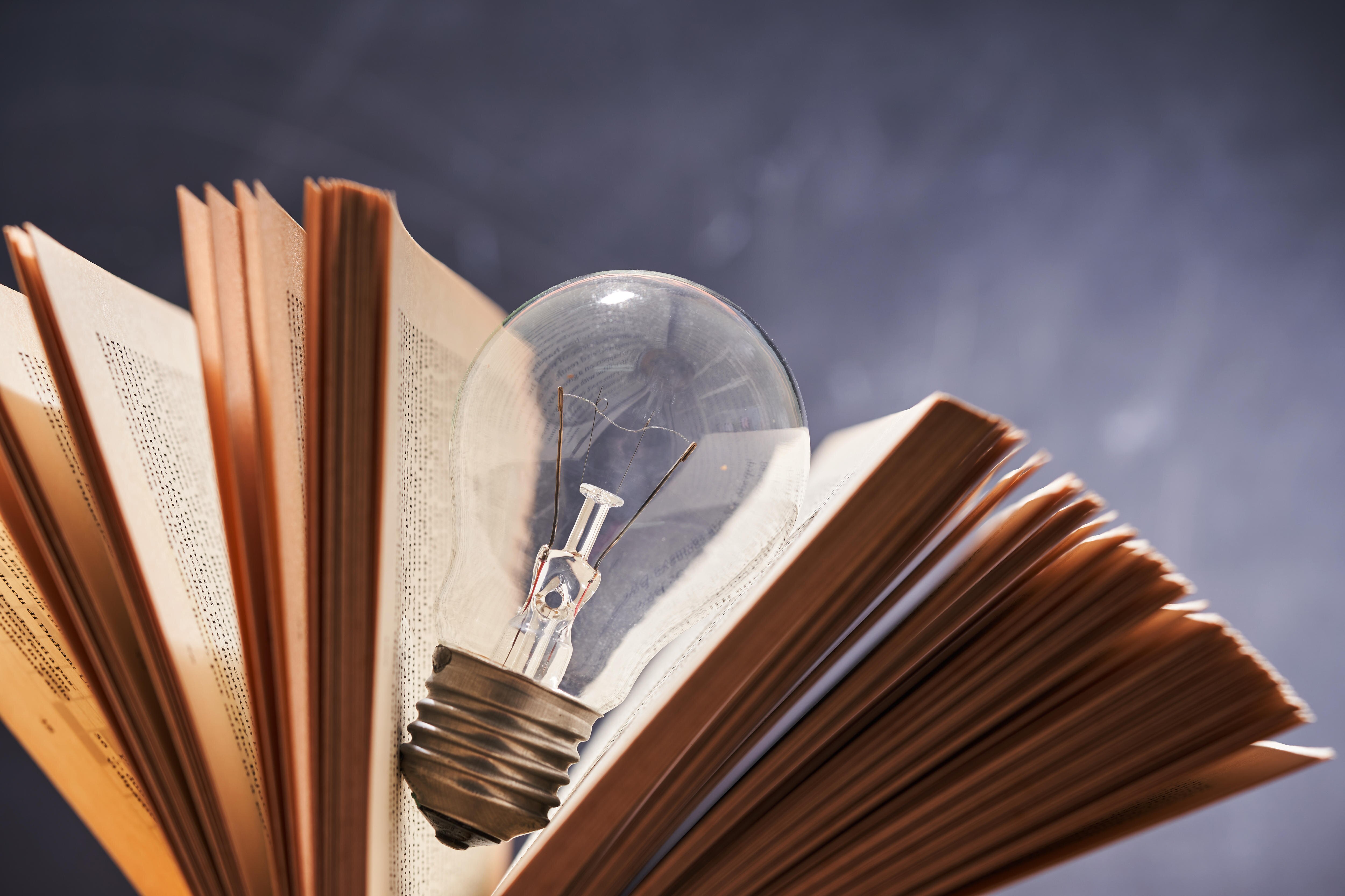A glass light bulb embedded in the middle of the yellowing pages of an old book