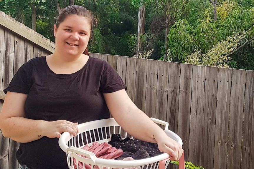 A woman holds a basket full of washing near a clothes line, for a story about the climate impact of washing clothes.