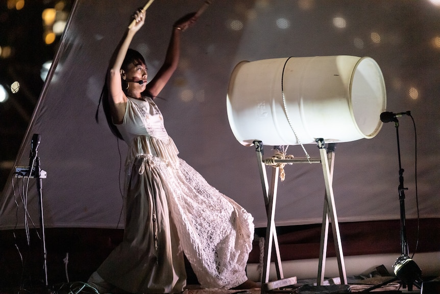 A woman performing on a boat wearing all white, playing a white drum