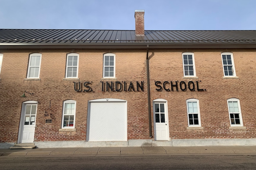 A brick building with white hopper windows and the large metal sign reads "US Indian School" displayed 