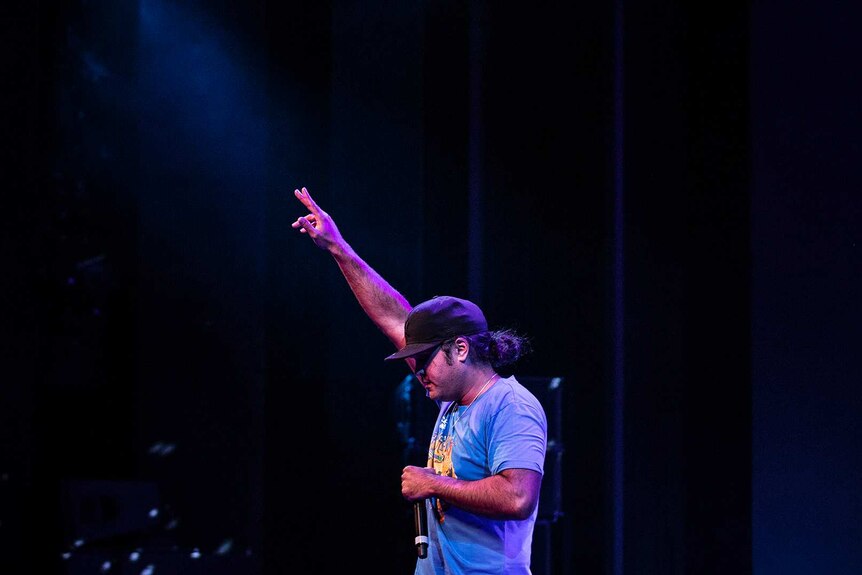 Colour photo of rapper Birdz looking down and with on arm raised while performing on stage at Sydney Opera House.