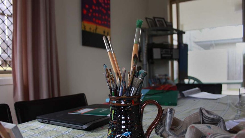 Jar of paint brushes on the kitchen table. Flickers of paint on the jar.