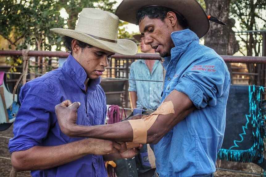 A ringer fixed supportive tape on the arm of another ringer as they prepare for the bull ride at the Kununurra Rodeo.