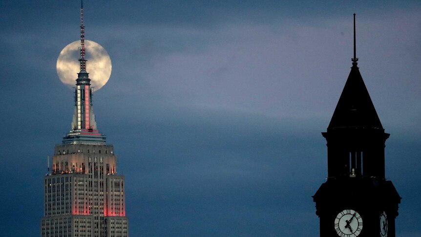 A large moon rises behind the Empire State Building