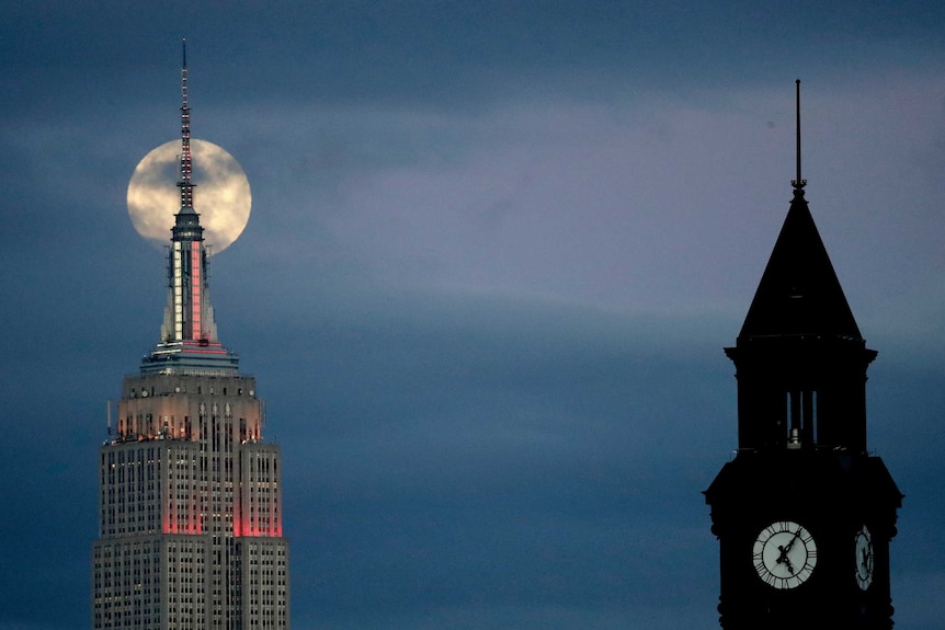A large moon rises behind the Empire State Building