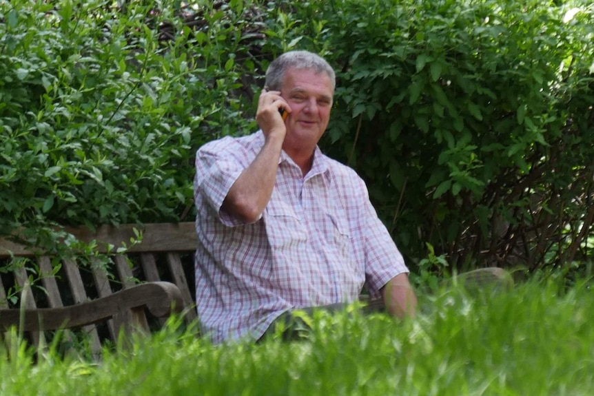 Ian Morgan sits on a bench and speaks on a mobile phone.