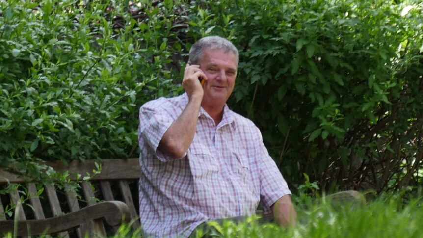 Ian Morgan sits on a bench and speaks on a mobile phone.