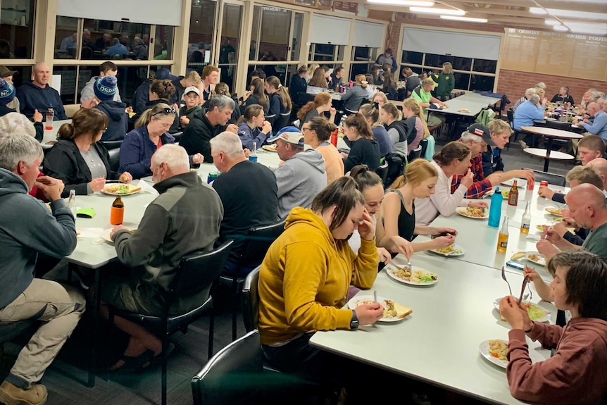 People eat meals at long tables inside a sports club.