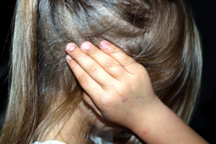 A generic child abuse image of a young girl unidentified holder her hand to her head.
