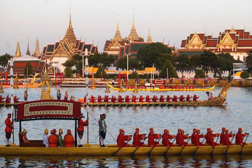 At dusk, you view a series of gold dragon boats on a river directly in front of Bangkok's ornate gold, Grand Palace.