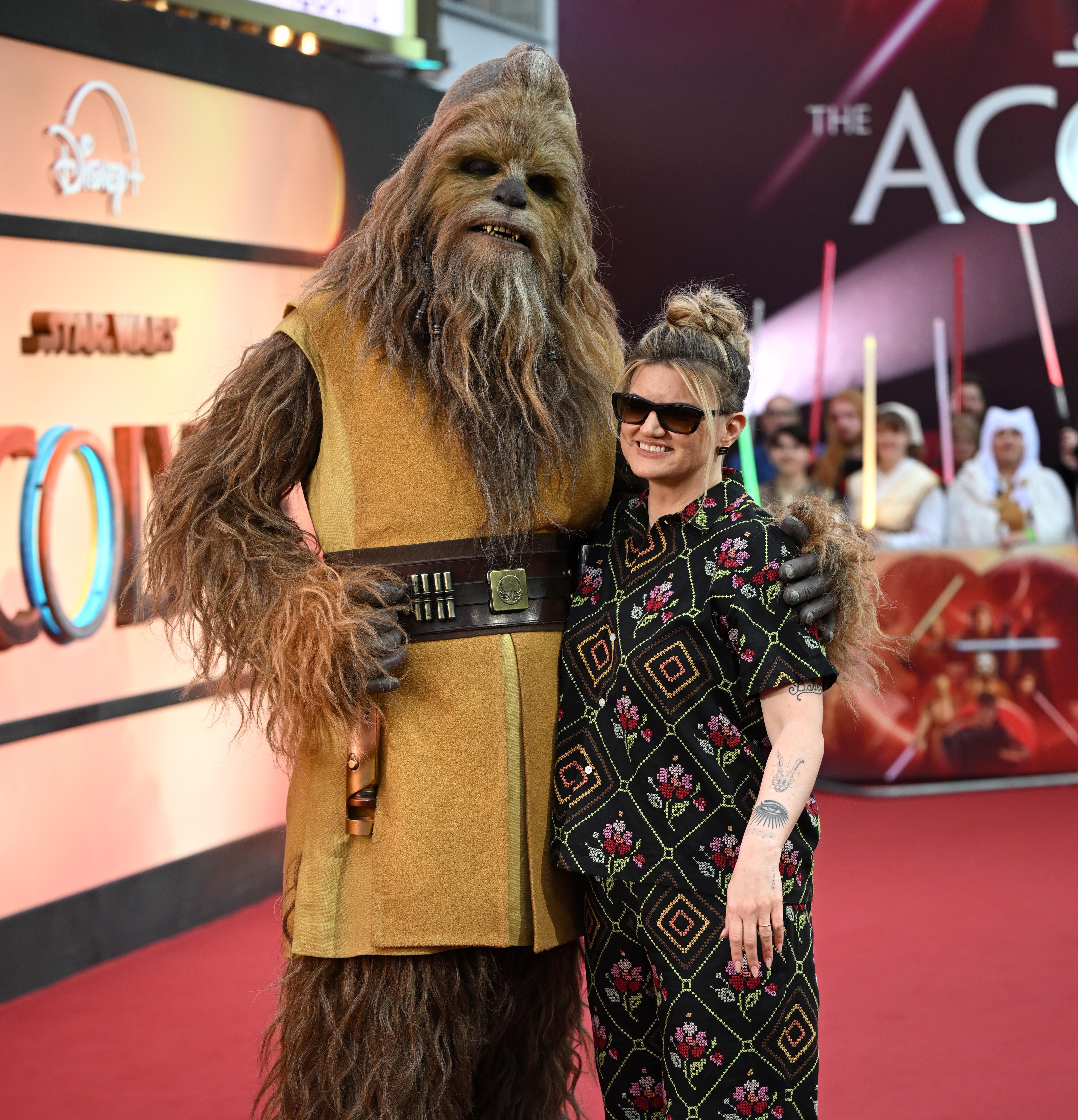 Leslye Headland in a cool outfit and sunglasses stands next to someone dressed as the wookiee