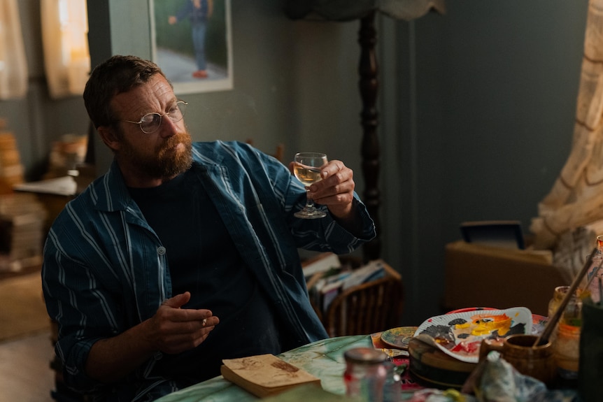 Simon, as Robert, smokes and drinks as he paints in his living room.
