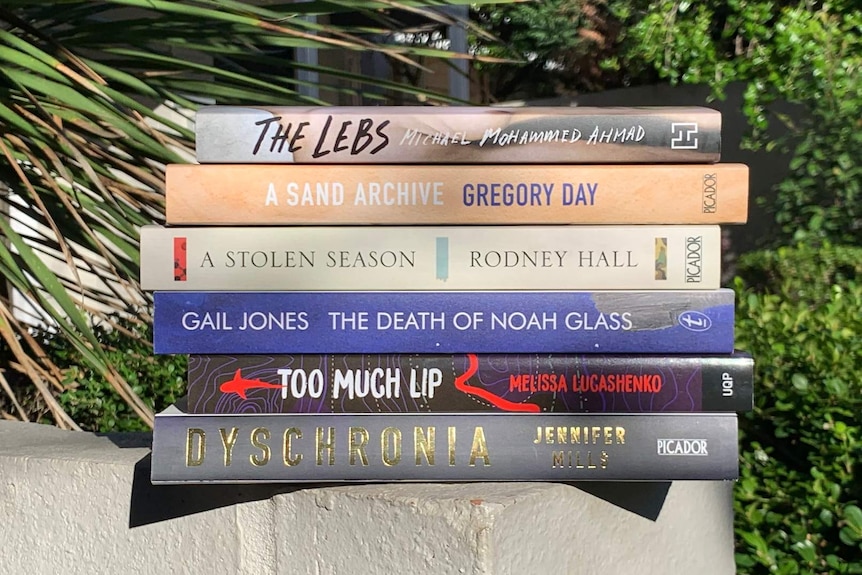 The shortlisted books stacked on a ledge in front of some greenery.