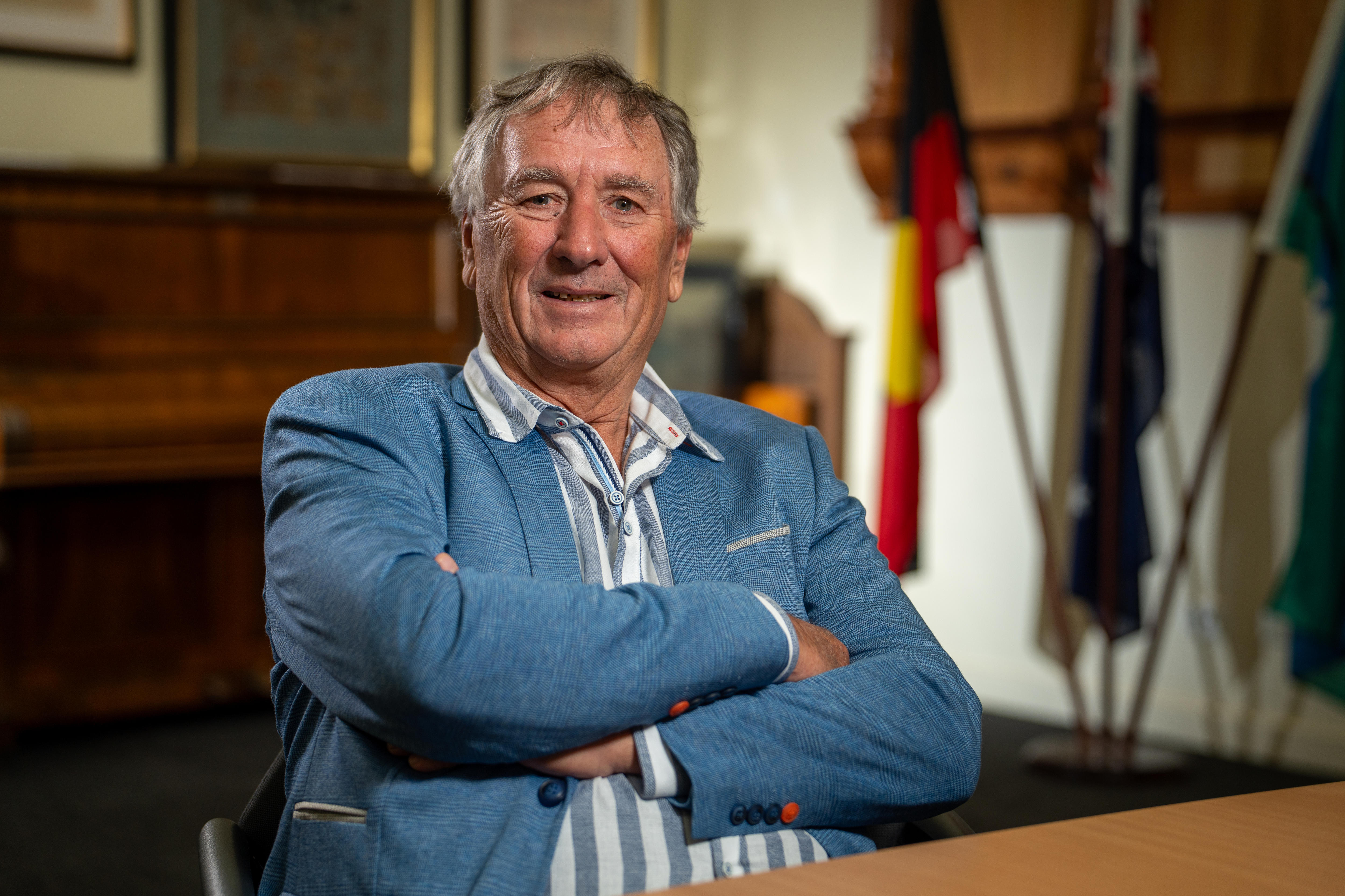 A man sits with his arm crossed, smiling.