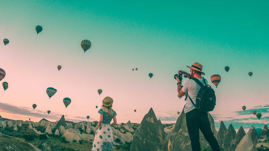 A man and a woman look at a landscape with dozens of hot air balloons