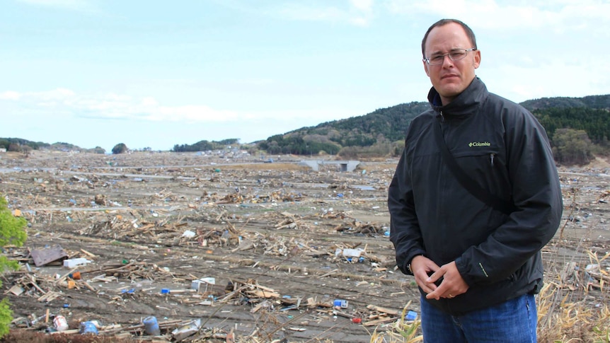 Mark Willacy stands with devastation from tsunami in the background