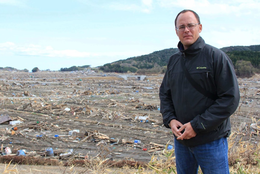 Mark Willacy stands with devastation from tsunami in the background