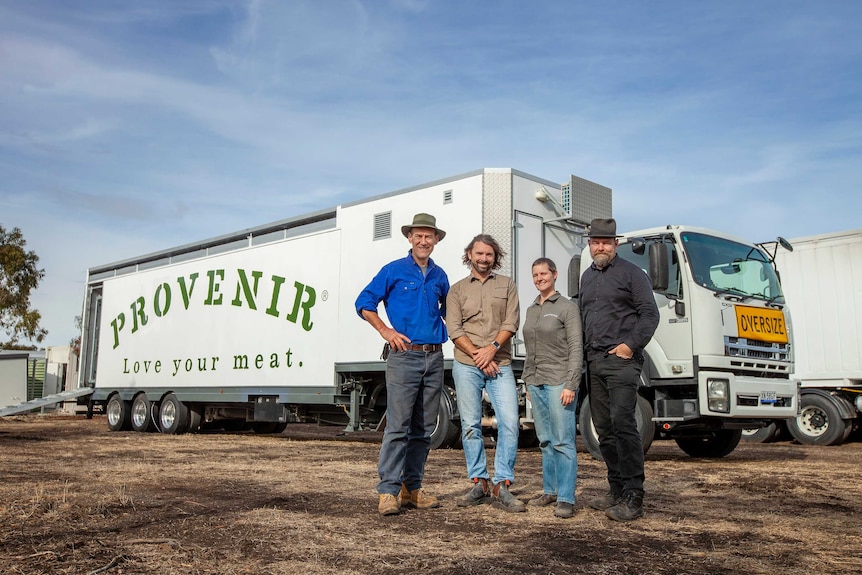 Four people stand in a row, grinning in front of a truck containing a mobile abattoir