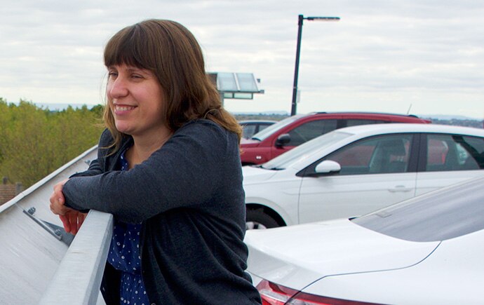 A woman leans on a railing at a car park.