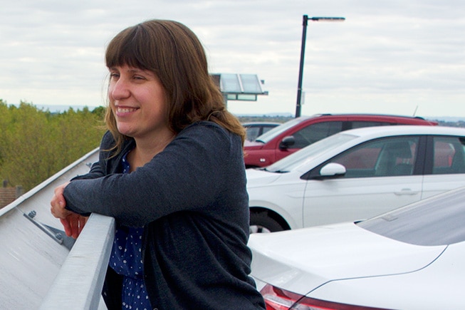 A woman leans on a railing at a car park.