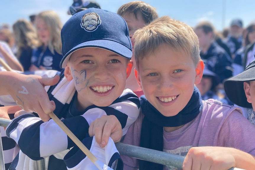 Cas Kovac and his friend smile in the sunshine, dressed in their blue and white Geelong team colours.