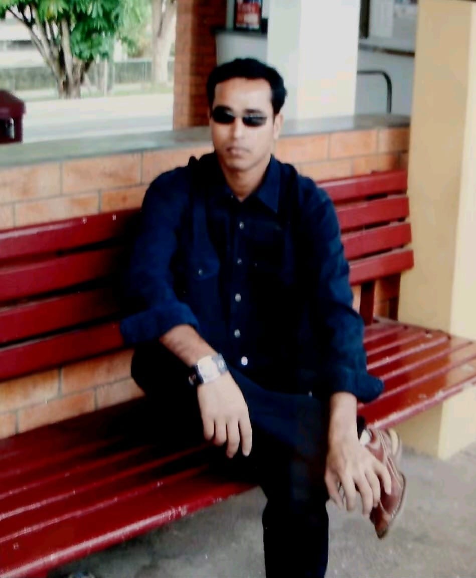 A man wearing sunglasses and a dark blue shirt sitting on a bench outside