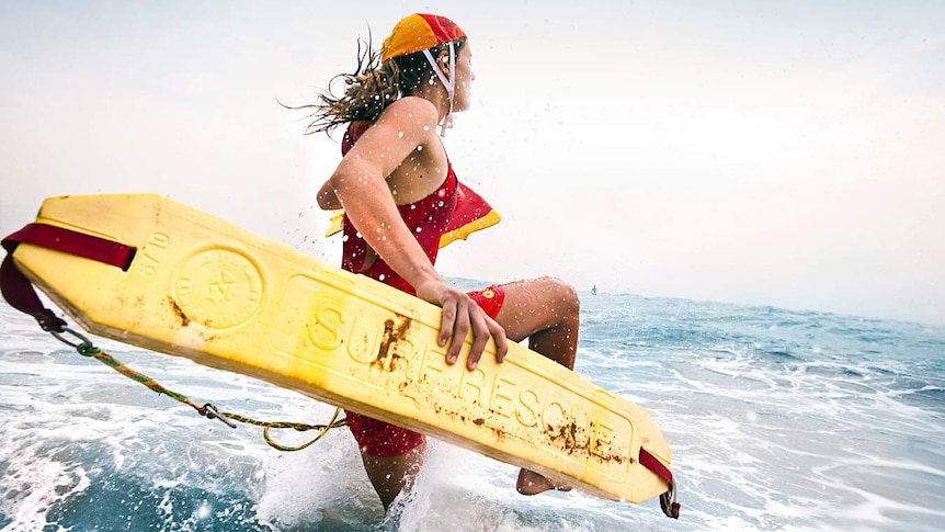 A surf lifesaver carrying a rescue board races into the ocean.