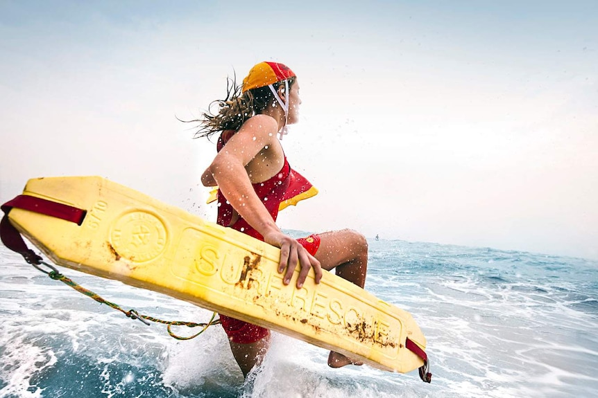 An unidentified woman runs into the surf with a lifesaving flotation device, wearing a red and yellow cap.