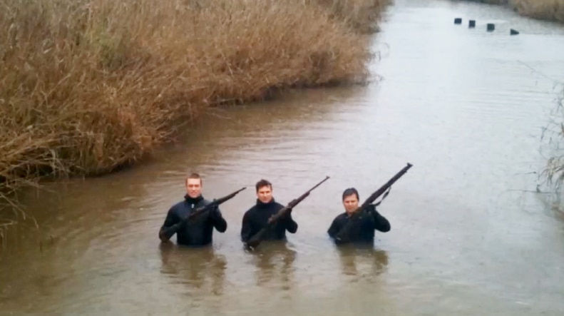 Three police divers holding up firearms they recovered in a river.