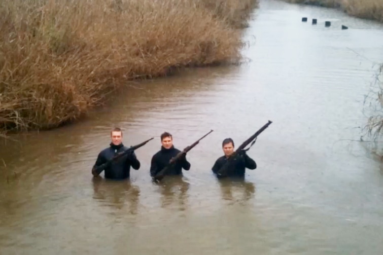 Three police divers holding up firearms they recovered in a river.