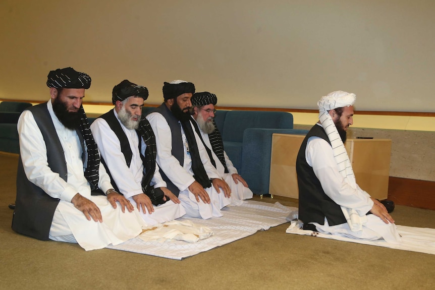 Afghanistan's Taliban delegation kneel on the floor to pray.