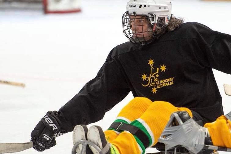 Australian Para-ice hockey athlete Darren Belling competing in a game at an ice rink, wearing a helmet with a go-pro camera.