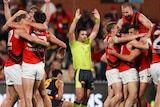 Essendon players celebrate will an umpire signals for full-time