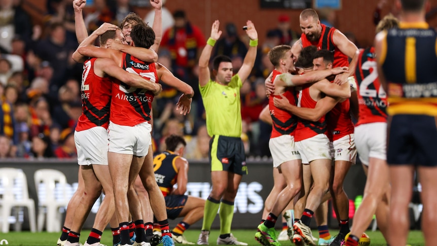Essendon players celebrate will an umpire signals for full-time