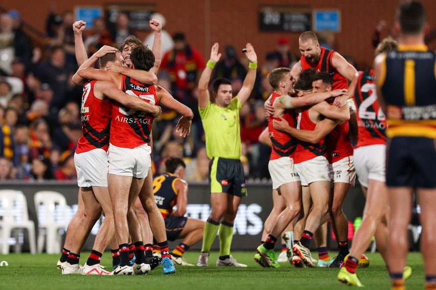 Essendon players celebrate will an umpire signals for full-time