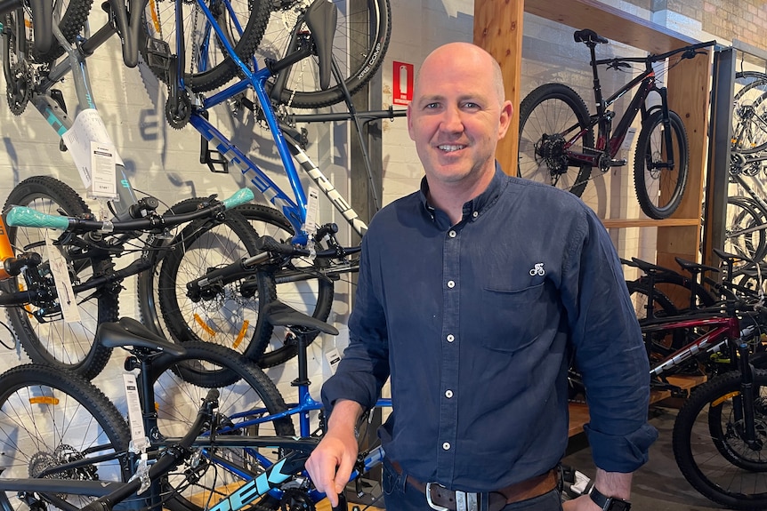 A man standing in a bike shop smiling at the camera. 