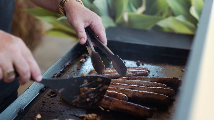 Close up of someone using tongs and an egg flip to ccok sausages on the bbq.