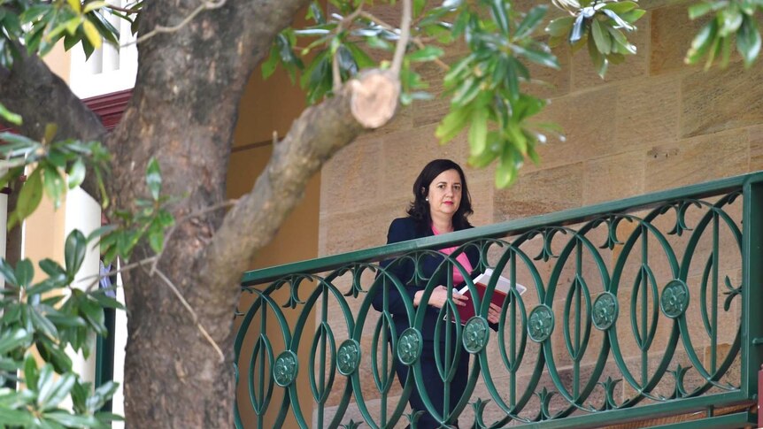 A woman in a pink top walk along a balcony holding papers.