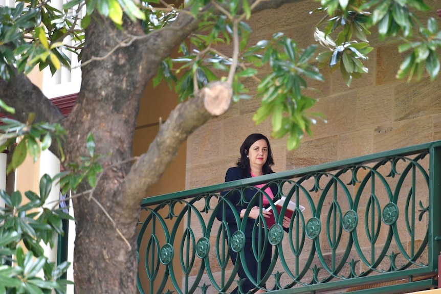 A woman in a pink top walk along a balcony holding papers.