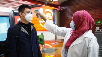 A woman in hijab takes a Chinese man's temperature at Dhaka airport.